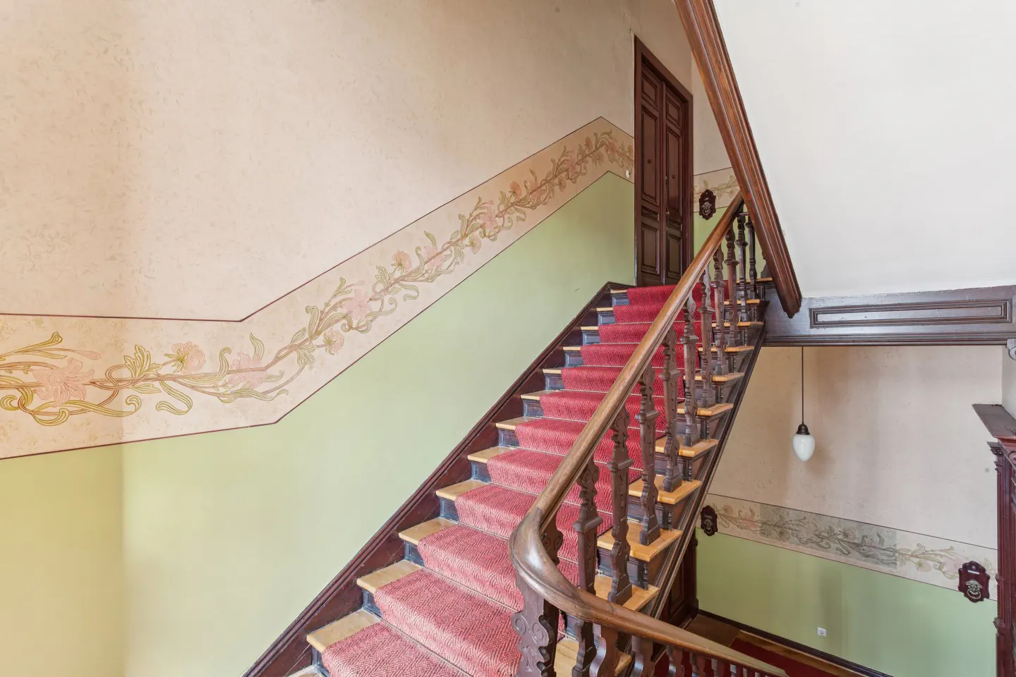 Interior view of a staircase with a red carpet, wooden banister, and decorative floral wall art.