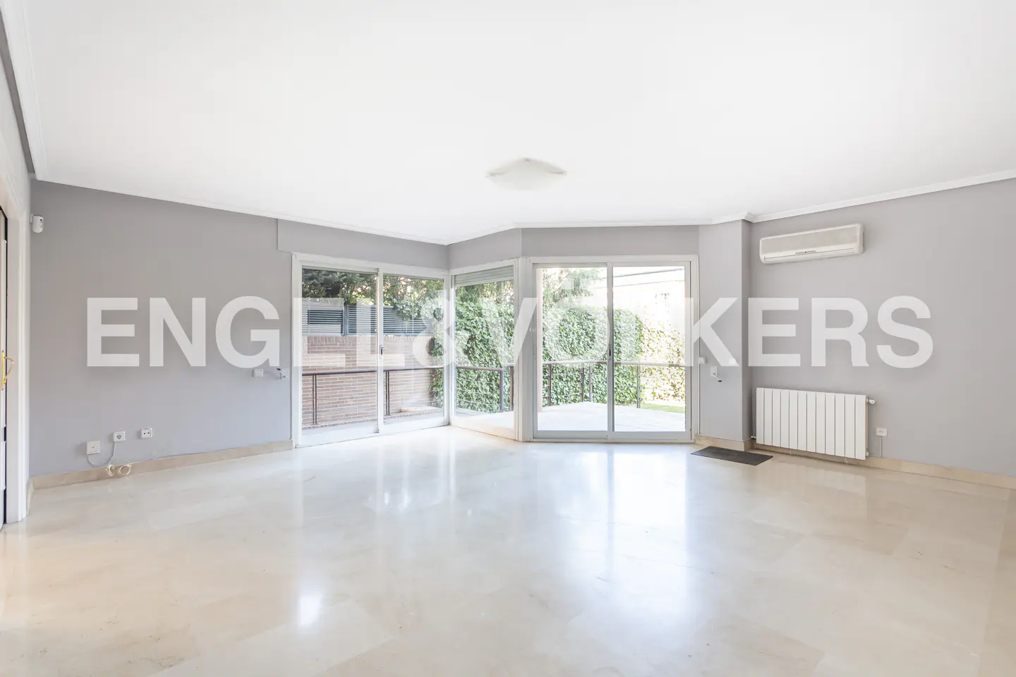 Bright, empty living room with gray walls, marble floors, and sliding glass doors to a green garden.