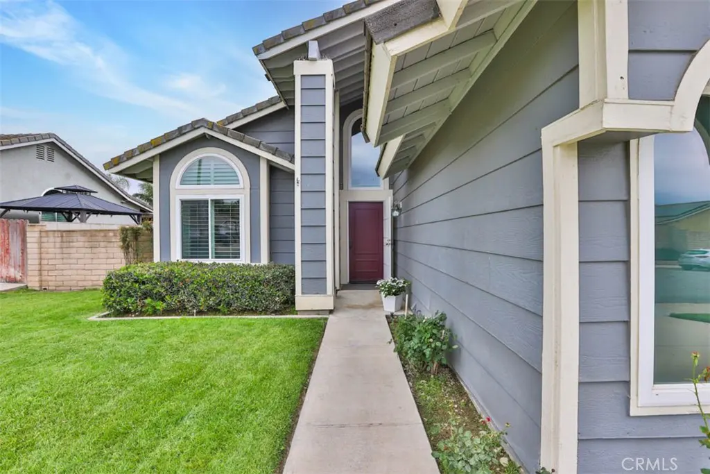 Exterior of a gray, single-story home with a red front door and green lawn.
