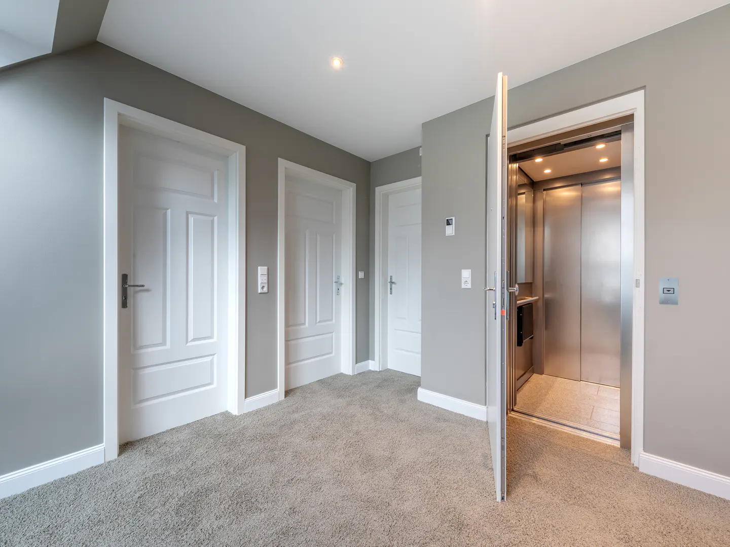 Hallway with gray walls, carpet, and white trim. Three white doors and an open elevator with a stainless steel interior.