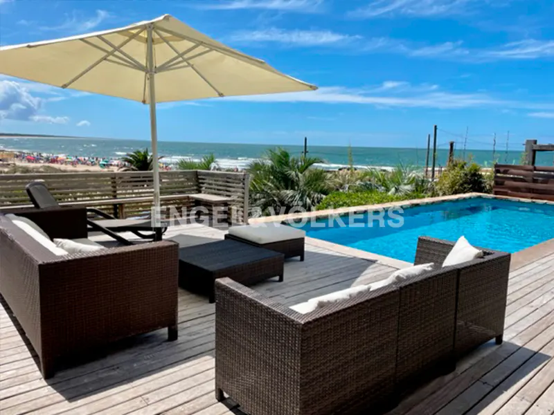 Outdoor patio with wicker furniture, a pool, and ocean view. A large umbrella provides shade over the seating area.