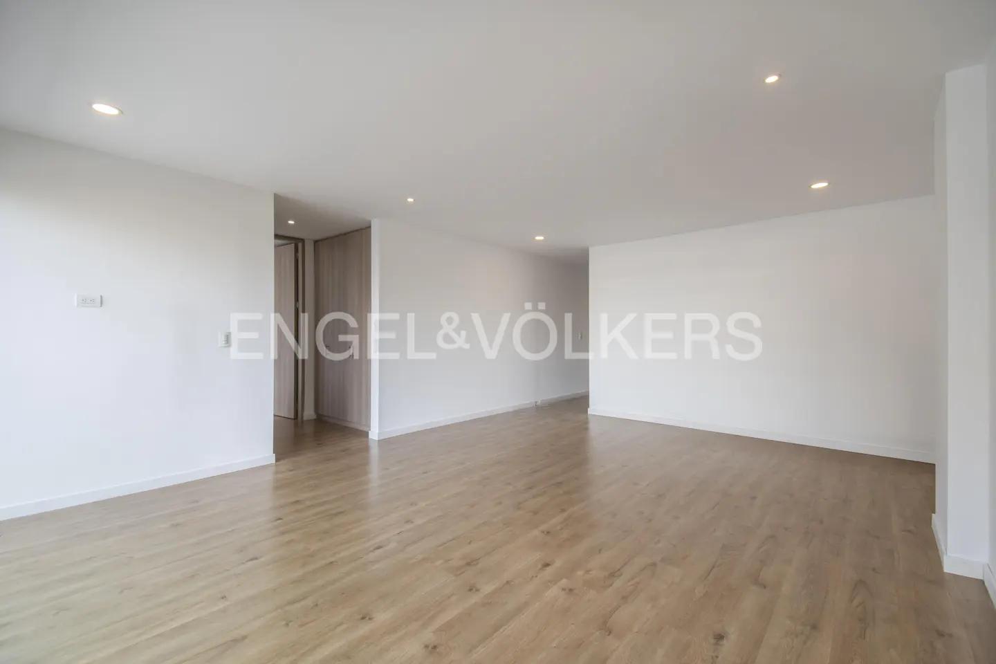 Bright, empty room with light wood floors and white walls. Engel & Völkers logo is visible.