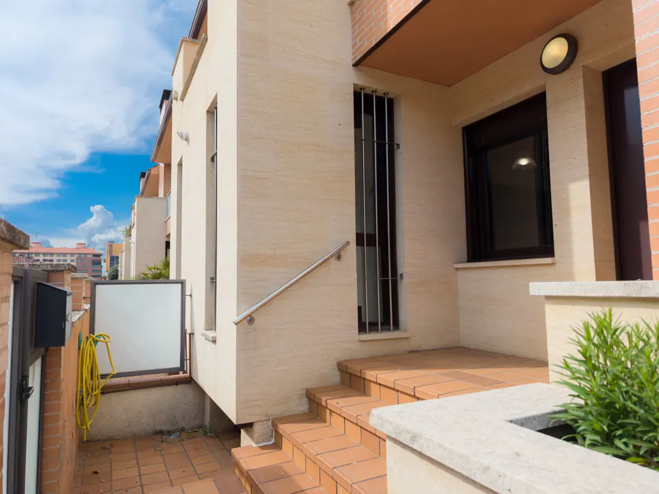 Exterior view of a beige building with brown steps leading to the entrance. A silver handrail is visible.
