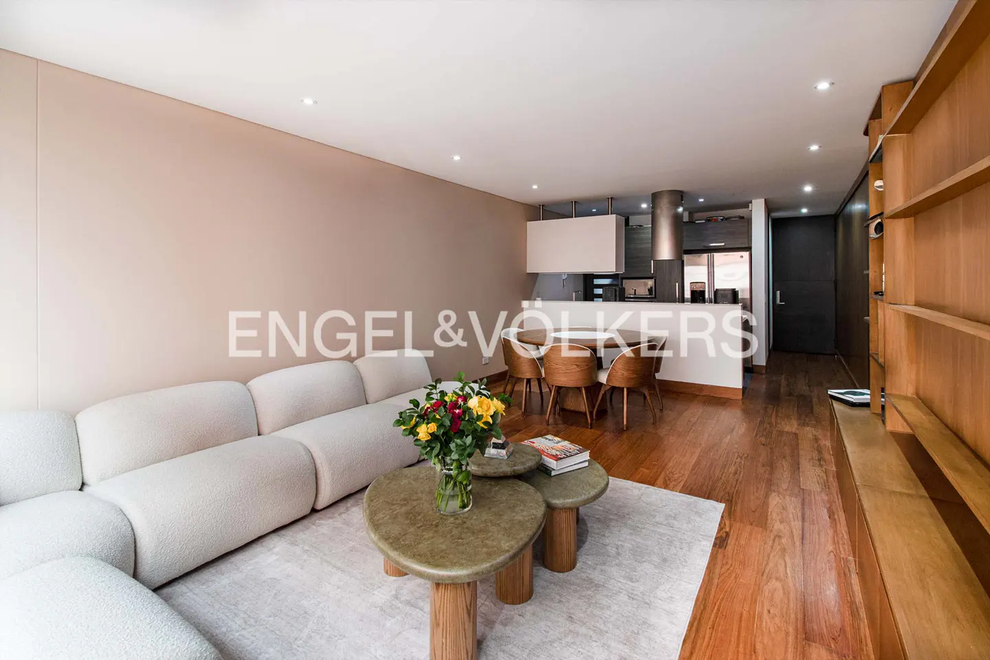 Modern living room with a white sectional sofa, two round coffee tables, a dining area, and wooden shelving on hardwood floors.