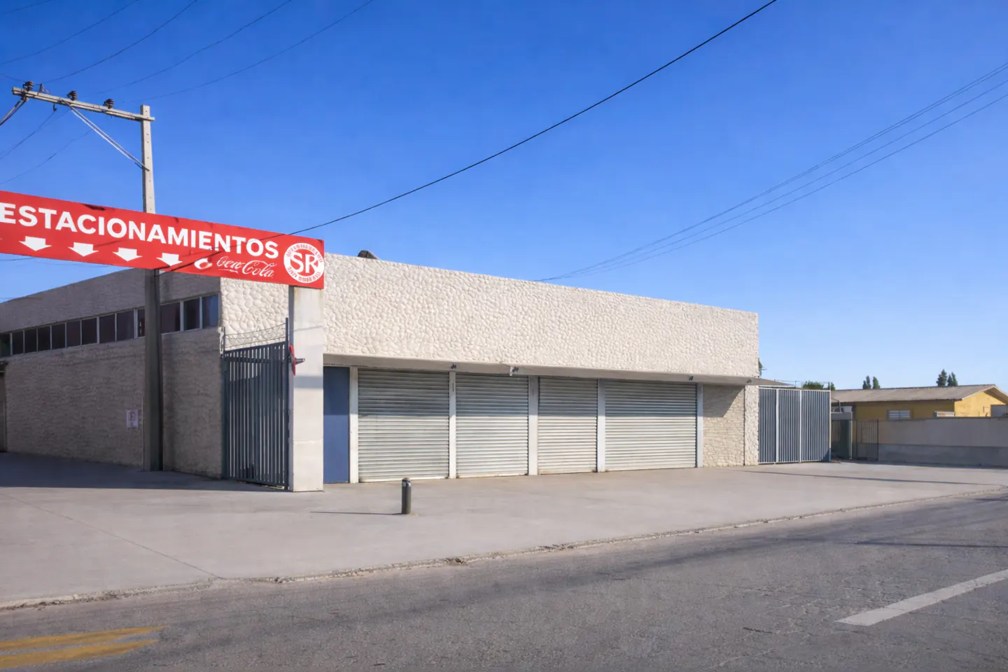 A one-story commercial building with closed metal roll-up doors and a "Estacionamientos" sign.