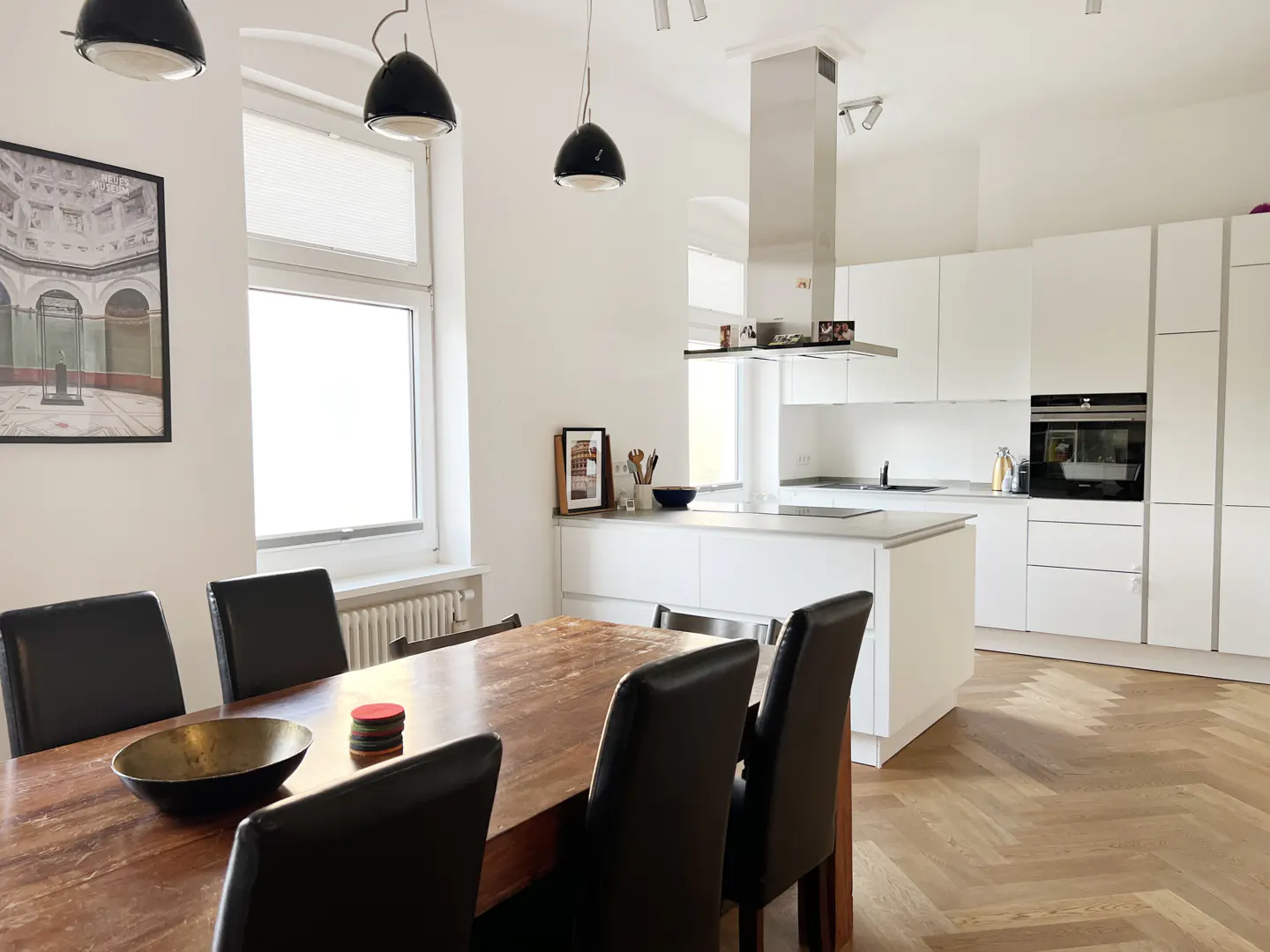 Bright, modern kitchen and dining area with white cabinets, stainless steel appliances, and a wooden table with black chairs.