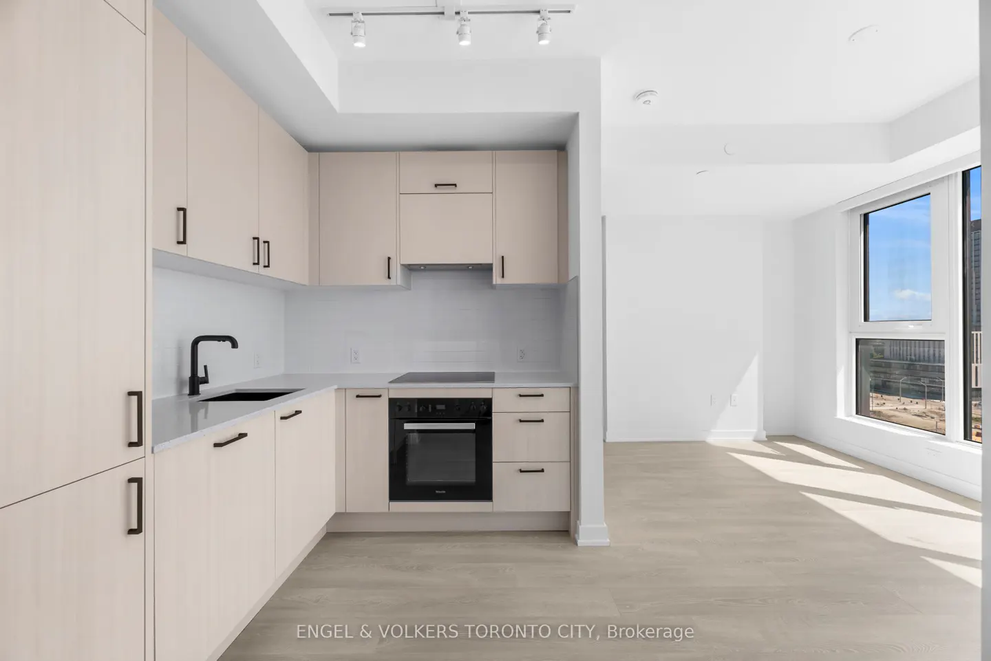 Modern kitchen with light wood cabinets, black hardware, white countertops, and large windows in an open-concept condo.