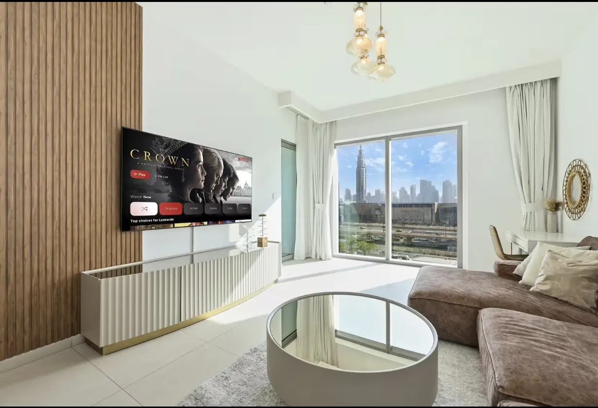 Living room with a TV playing "The Crown", a brown sofa, and a view of the Dubai skyline.