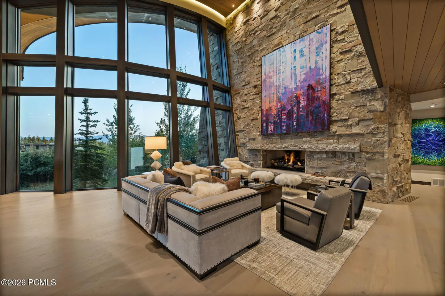 Living room with stone fireplace, large windows, and modern furniture. A colorful painting hangs above the fireplace.