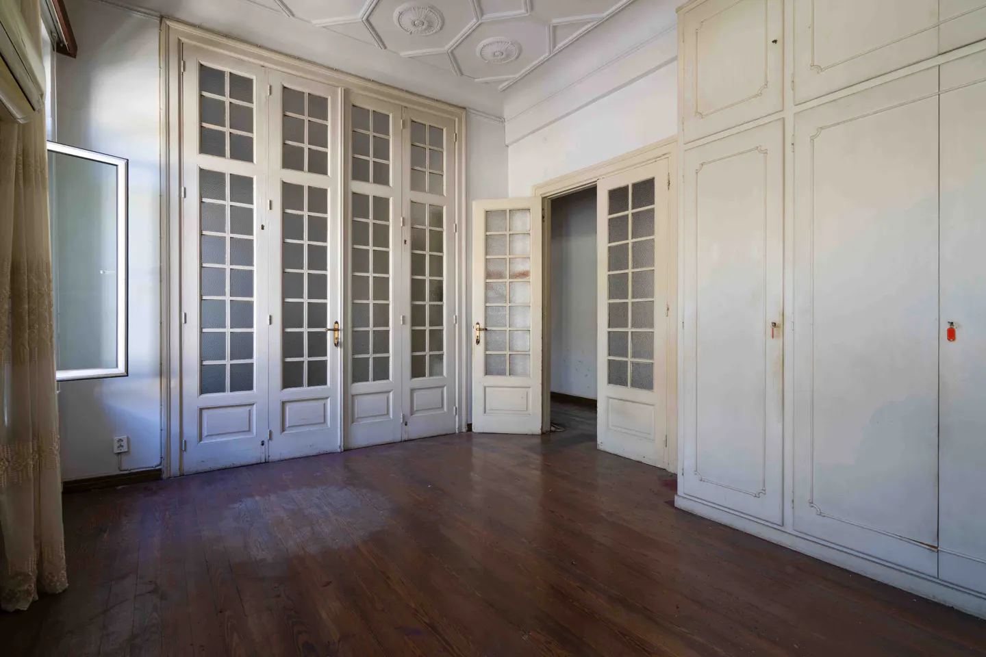 Empty room with hardwood floors, white walls, and tall white doors with glass panes. A large white wardrobe is on the right.