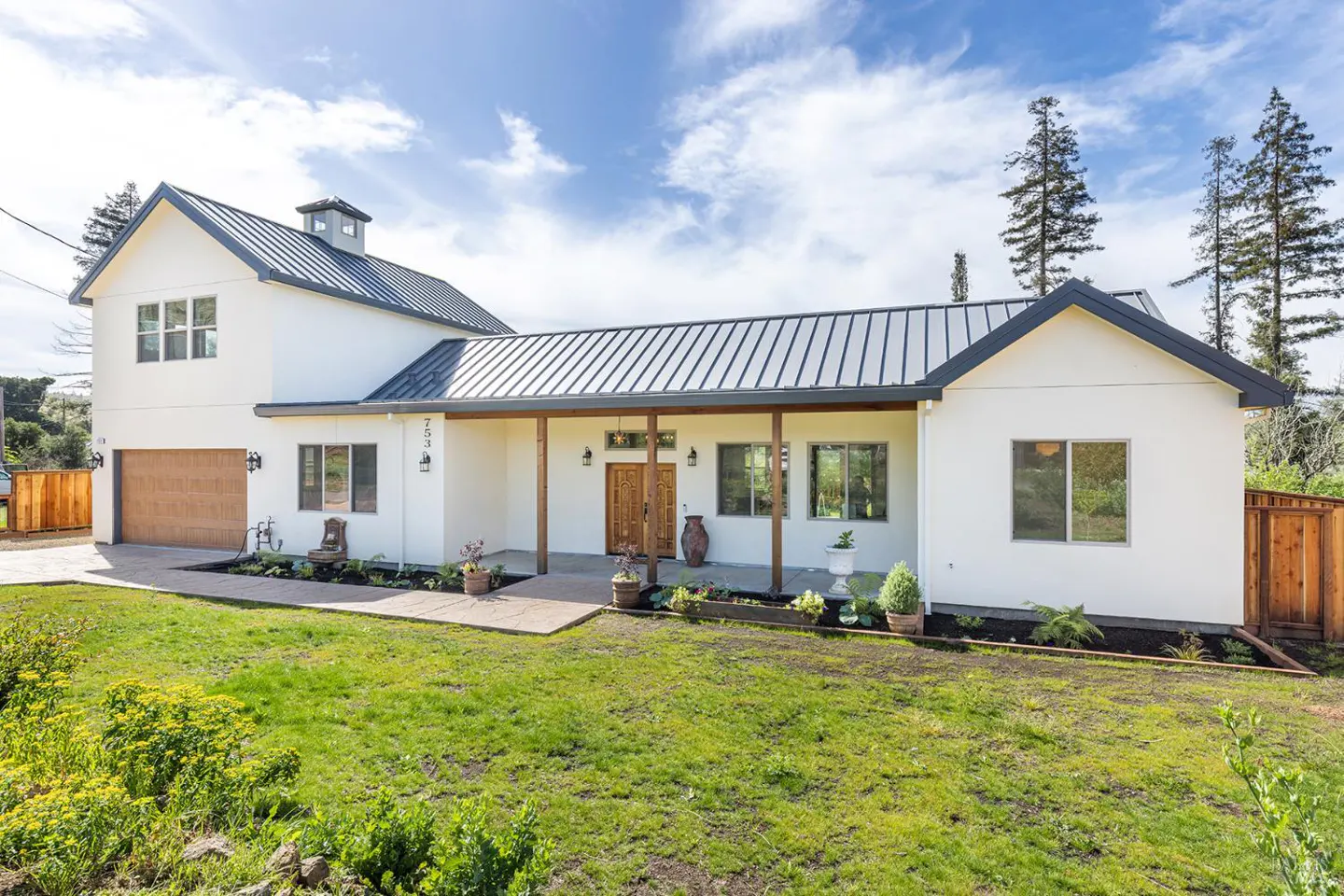 Exterior of a white, modern farmhouse with a metal roof, wooden porch columns, and a green lawn.