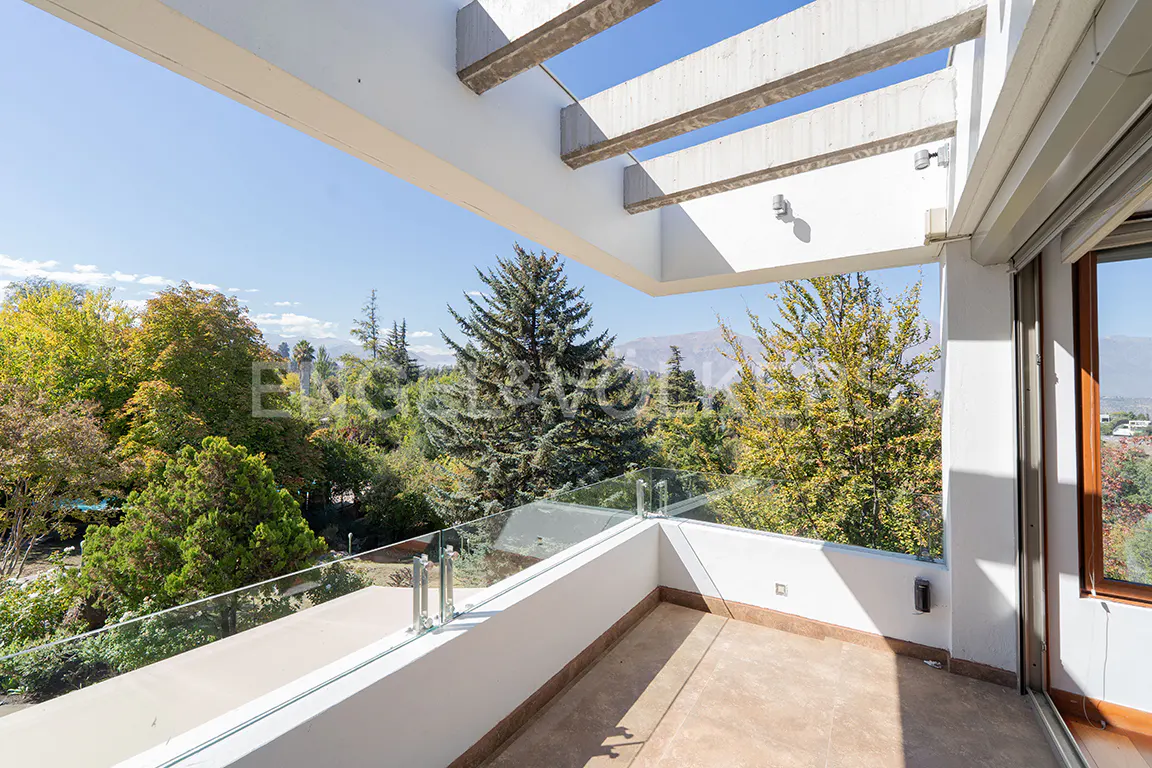 Balcony view with glass railing overlooking lush green trees and distant mountains under a clear blue sky.