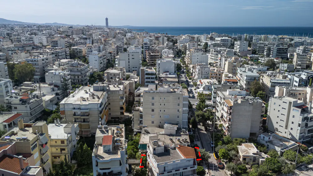 Aerial view of a dense city with white buildings, green trees, and the sea in the background.