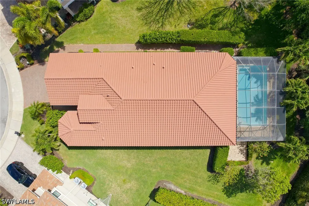 Aerial view of a house with a terracotta tile roof, a screened-in pool, and green lawn.