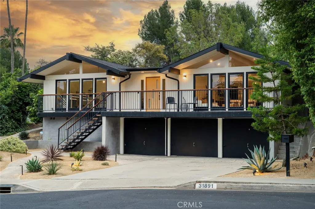 Modern two-story home with white siding, black trim, a large balcony, and a three-car garage at sunset.