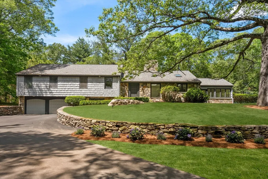 Exterior of a two-story house with gray shingles and stone, green lawn, and stone wall.