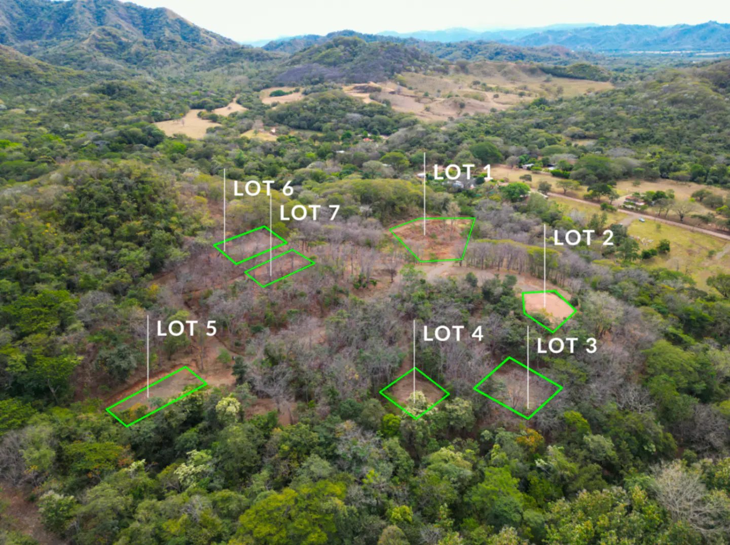 Aerial view of seven lots marked in green on a wooded hillside with mountains in the background.