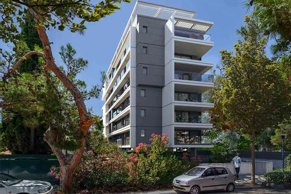 Modern six-story apartment building with white balconies and gray accents, surrounded by lush greenery and a parked silver car.