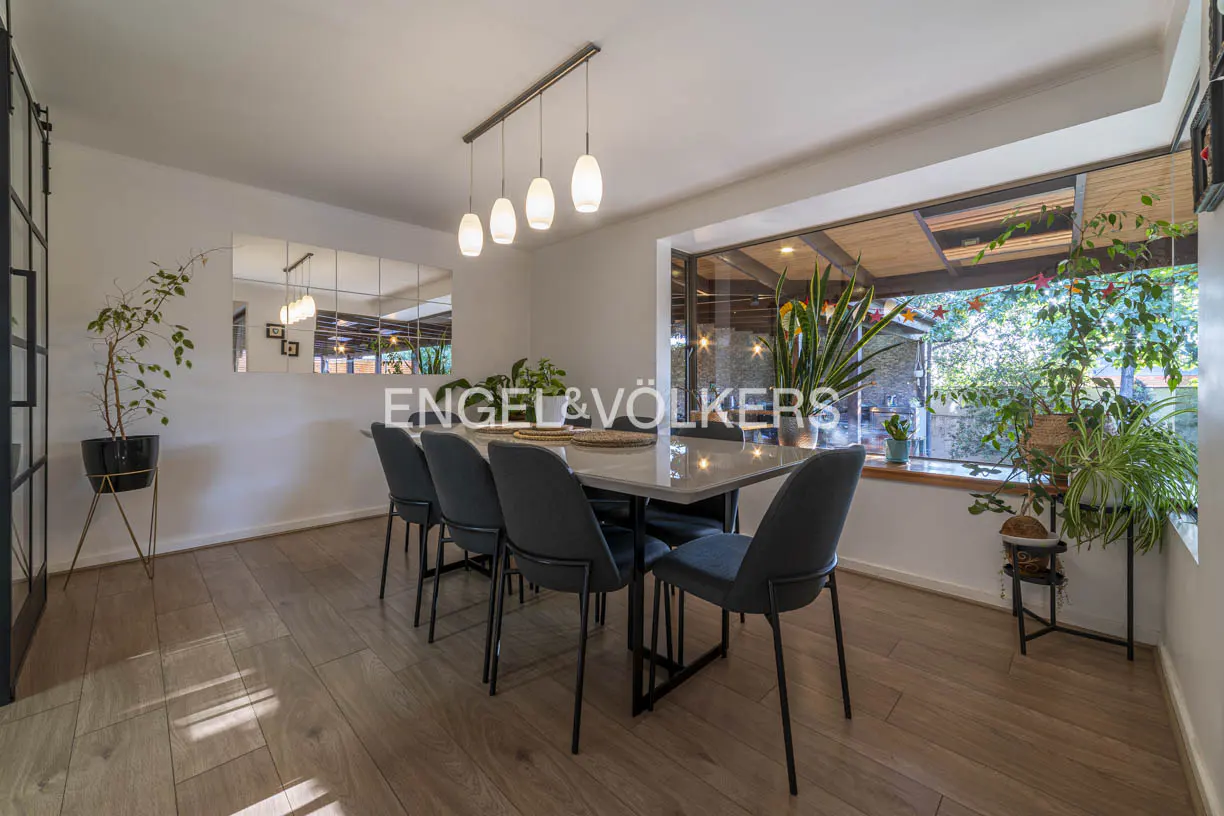 Bright dining room with wood floors, a marble table with six blue chairs, and a large window with plants.