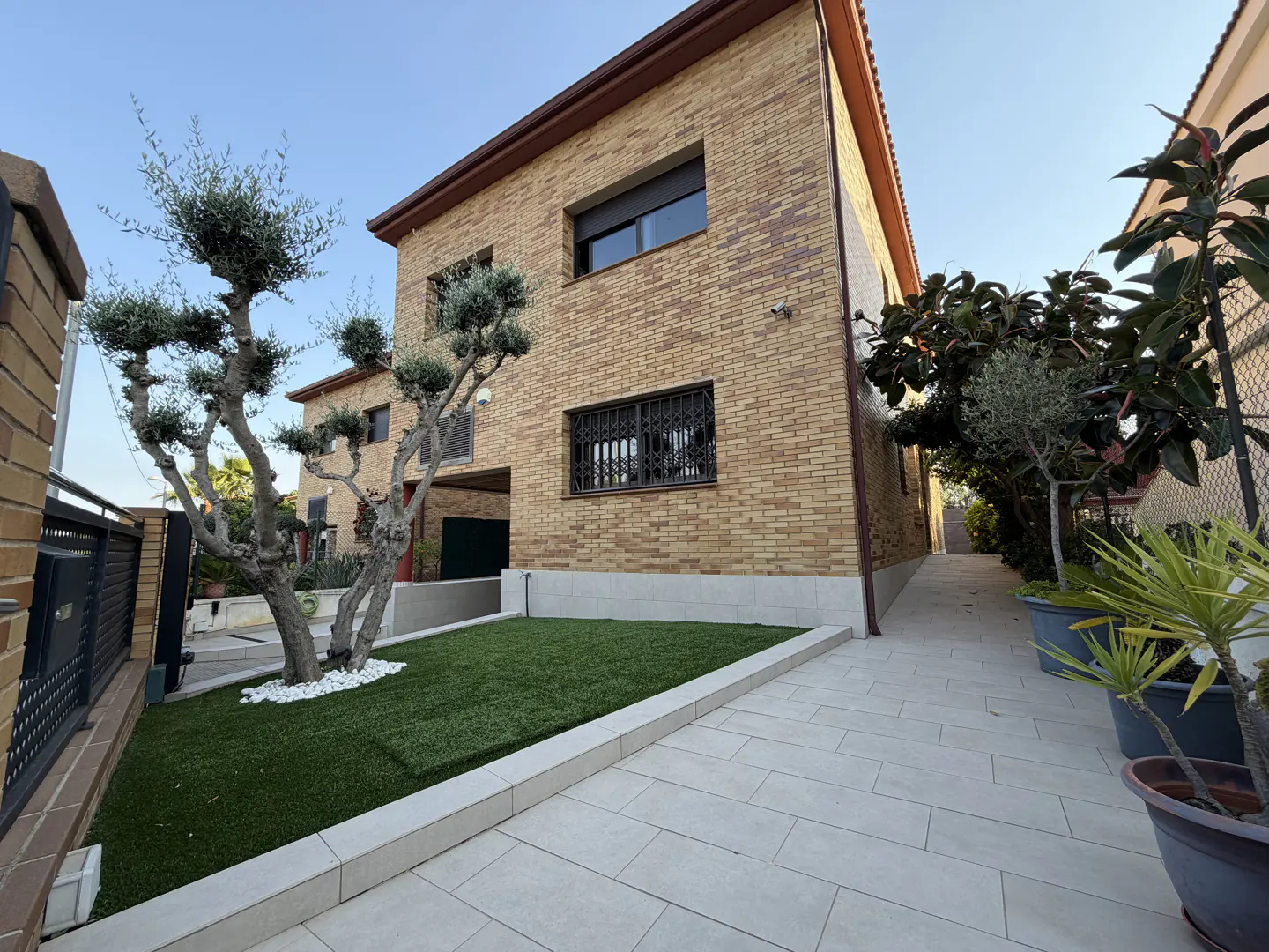 Two-story brick house with a small green lawn, a trimmed tree, and a stone walkway.