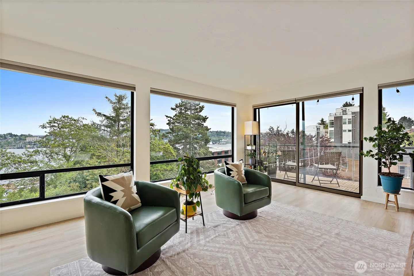 Bright living room with two green chairs, a patterned rug, and large windows with a view of trees and water.