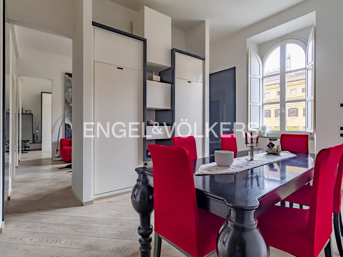A dining room with a black table, red chairs, and a window with white shutters.
