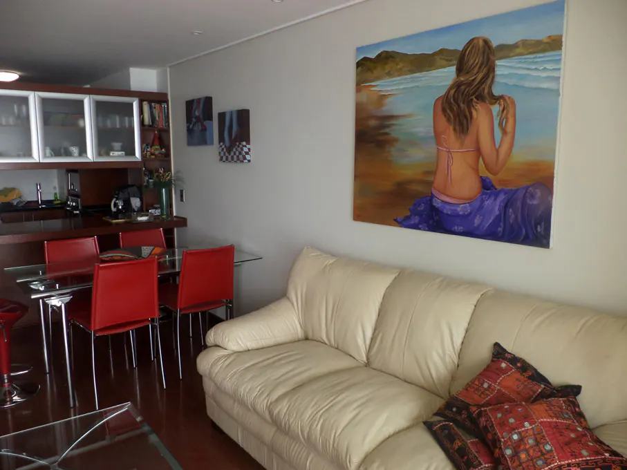 Living room with a cream sofa, red chairs at a glass table, and a painting of a woman on a beach.
