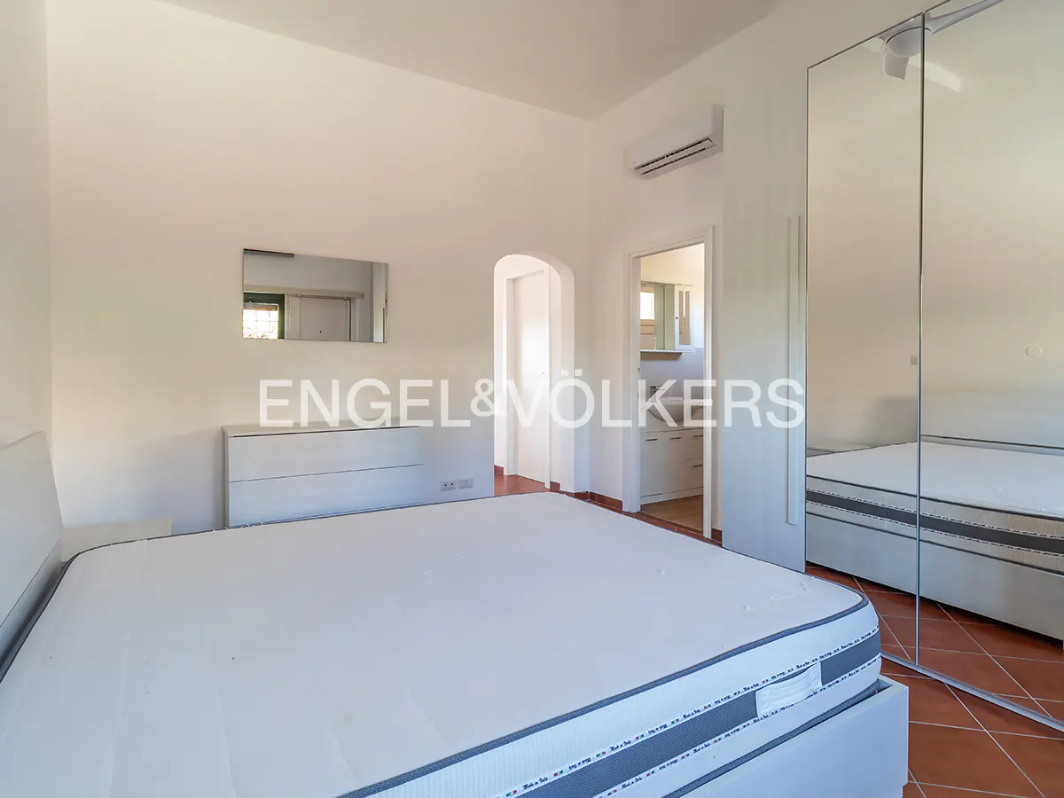 Bright bedroom with white walls, a large bed, mirrored closet, and a glimpse into an adjacent bathroom.