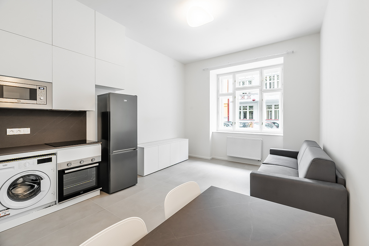 Modern studio apartment with white cabinets, black appliances, a grey sofa, and a dining table by a bright window. [AI-generated text]