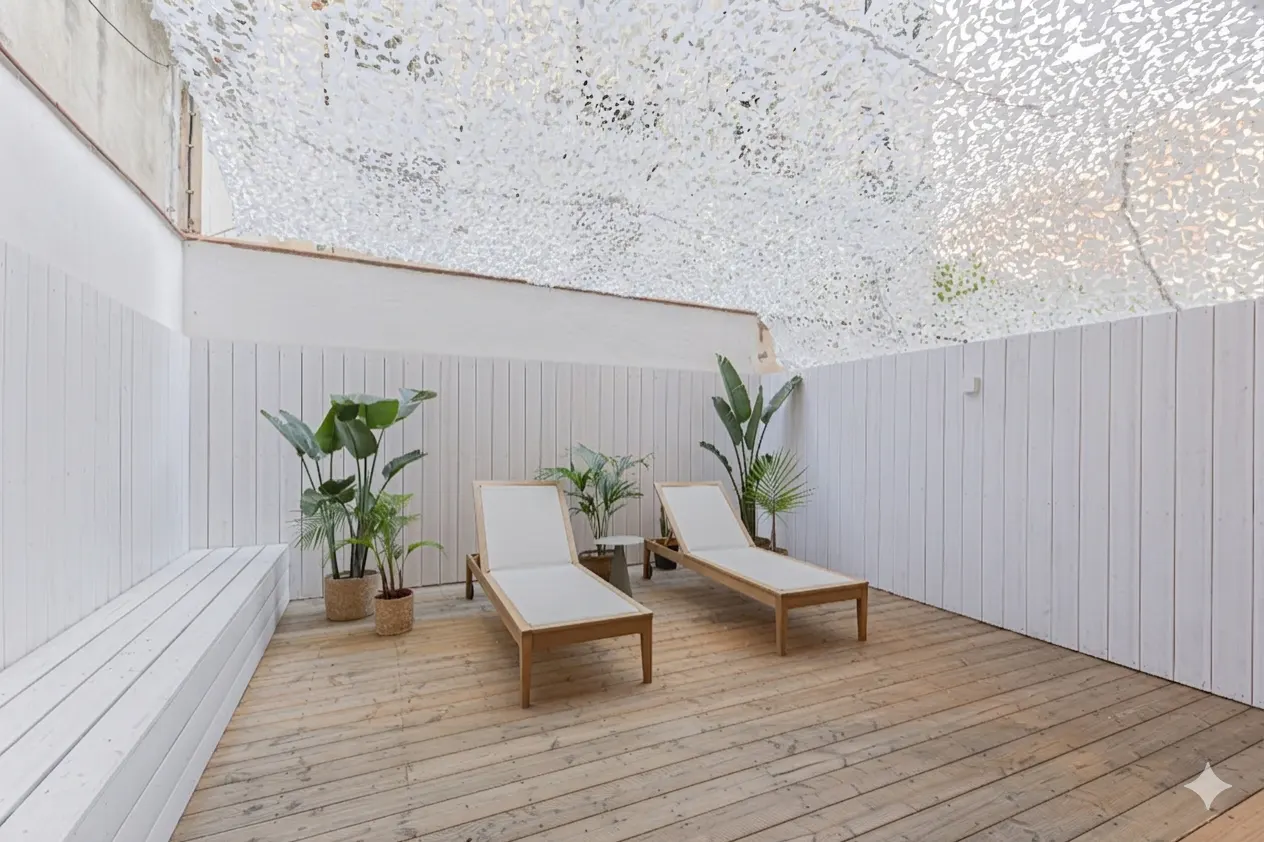 A wooden deck patio with two lounge chairs, potted plants, and white walls under a white camouflage shade net.