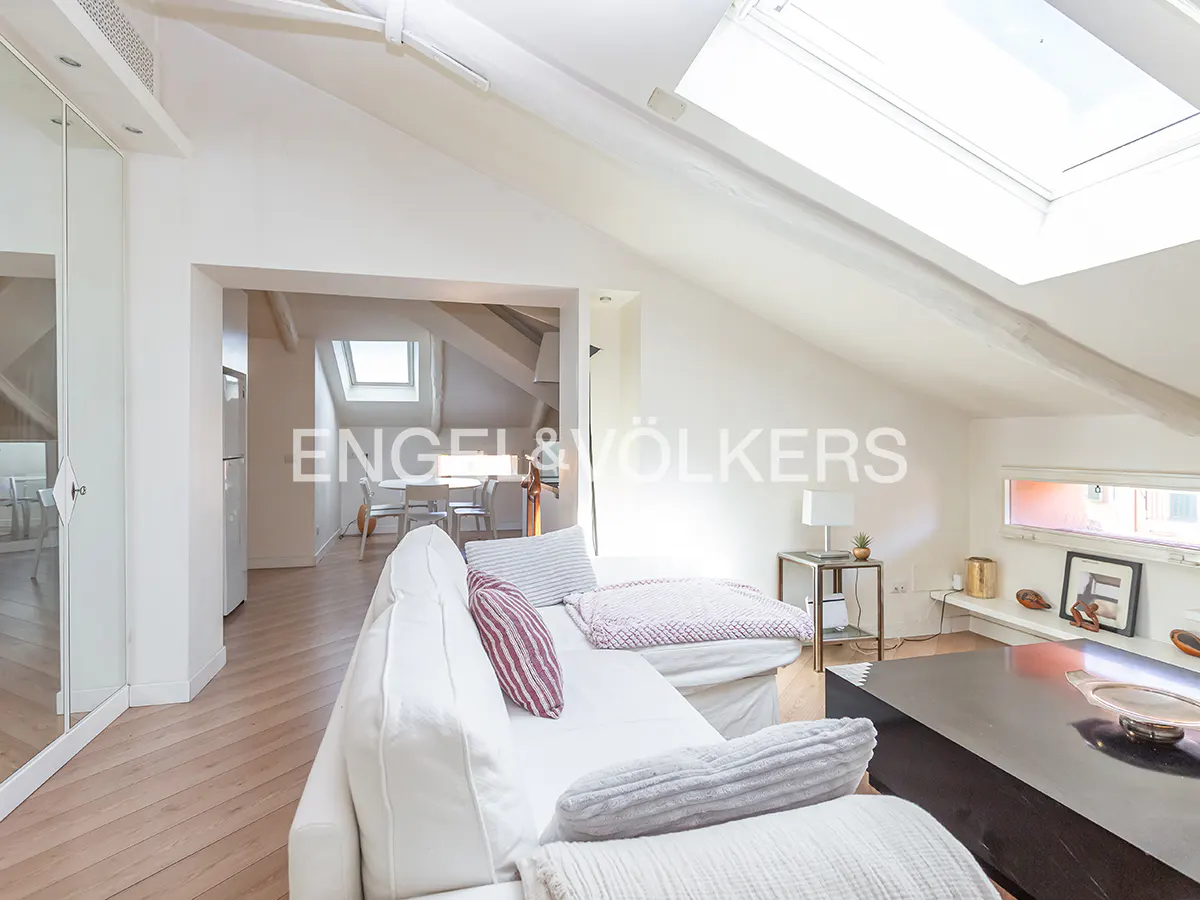 Bright attic living room with white sofa, skylight, wooden floors, and a view into a dining area.