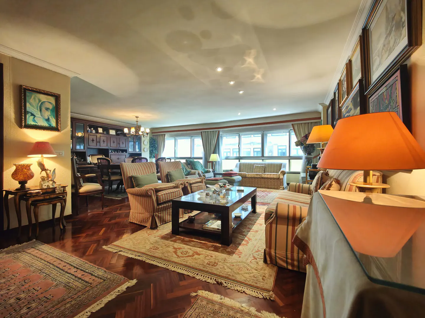 Spacious living room with striped armchairs, a dark wood coffee table, hardwood floors, and warm ambient lighting.