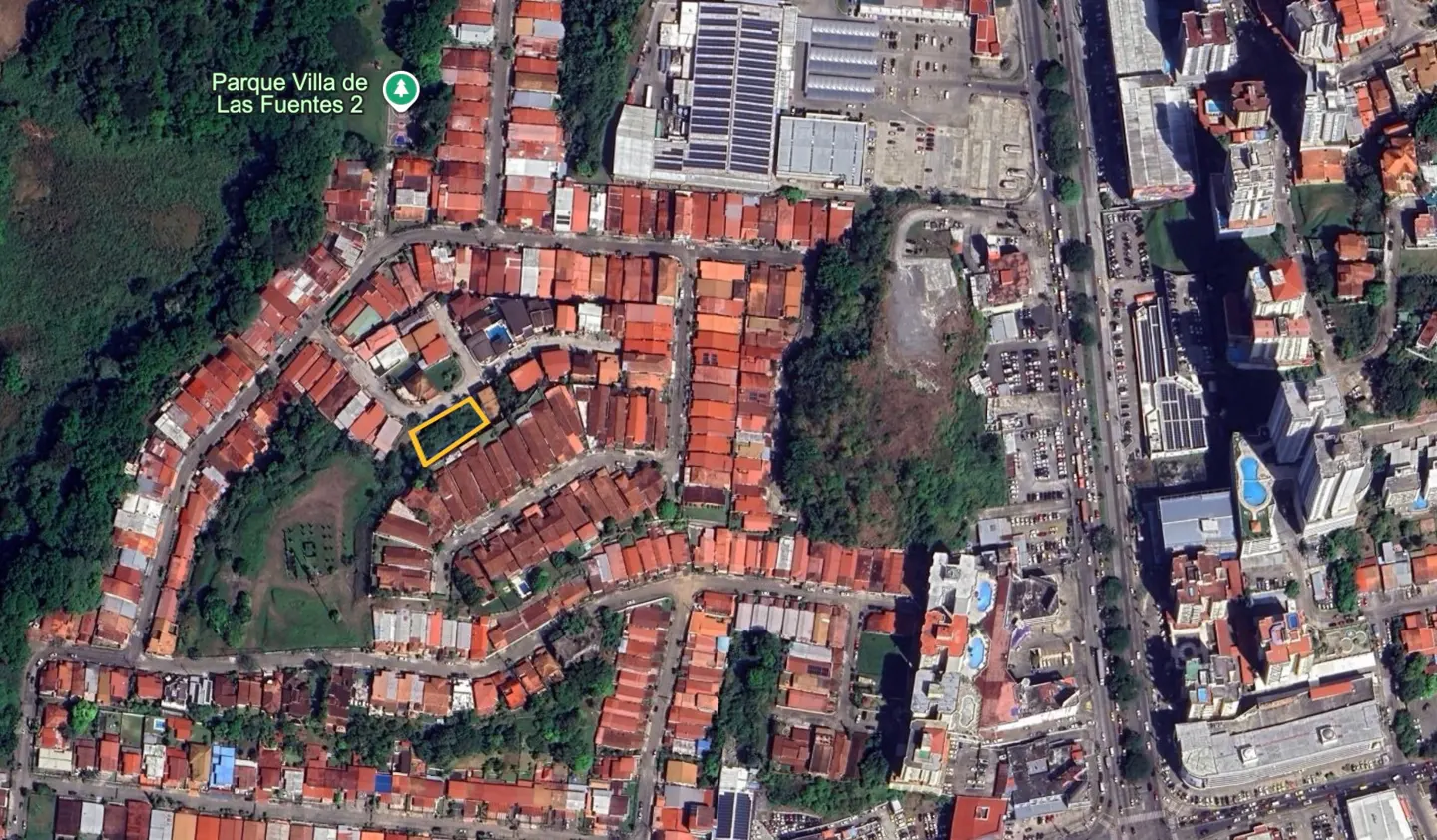 Aerial view of a residential area with red-roofed houses, green trees, and a yellow-outlined property.