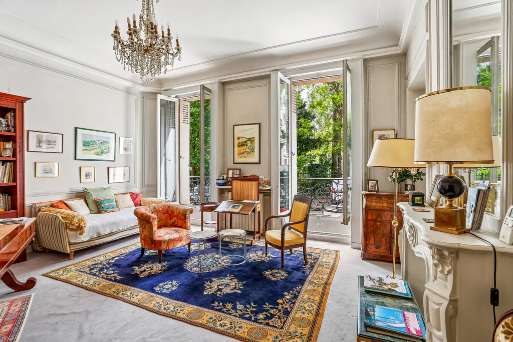 Elegant living room with open French doors, a crystal chandelier, and a blue floral rug.