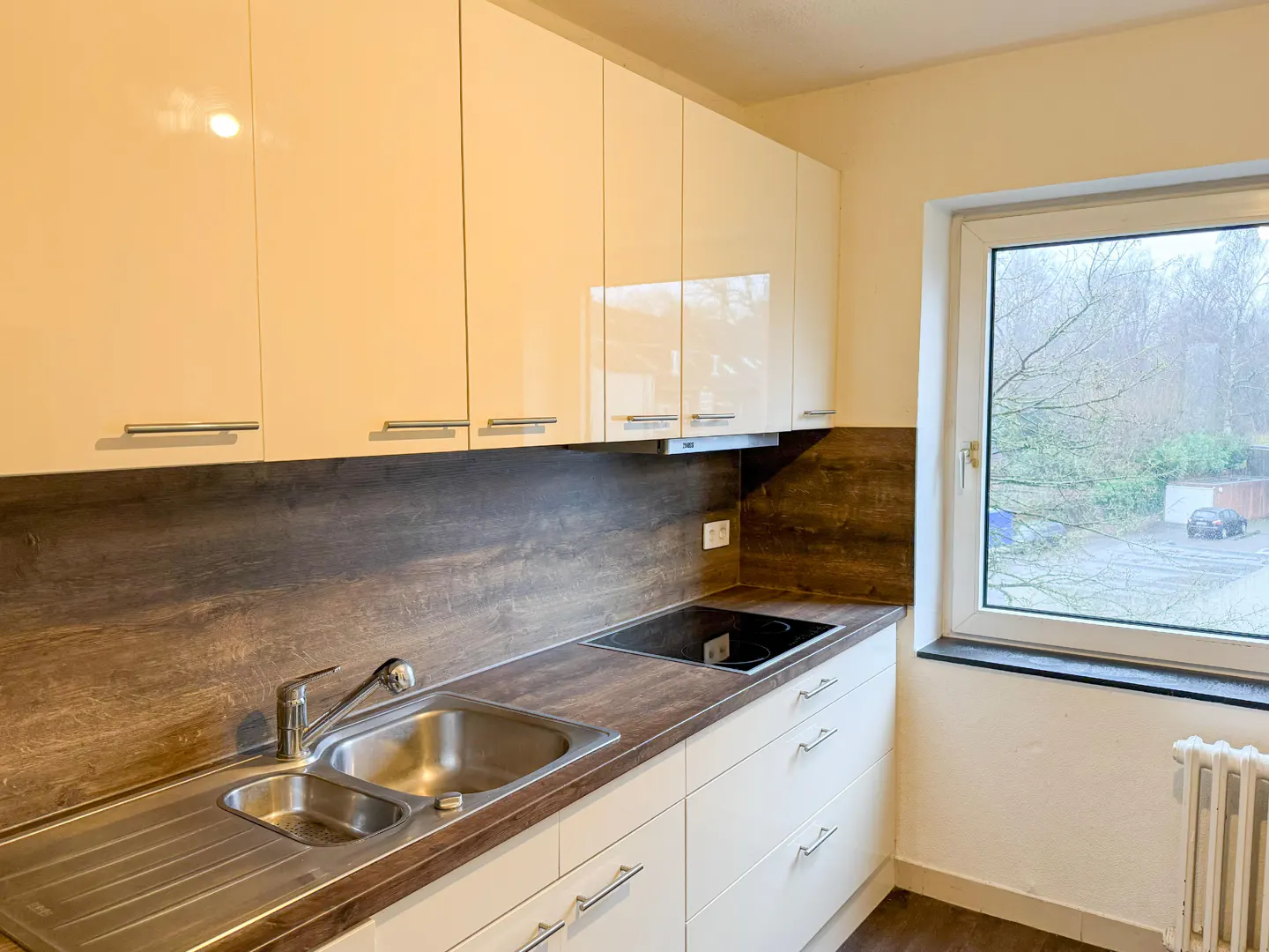 Bright kitchen with white cabinets, stainless steel sink, and dark countertop. A window overlooks trees outside.