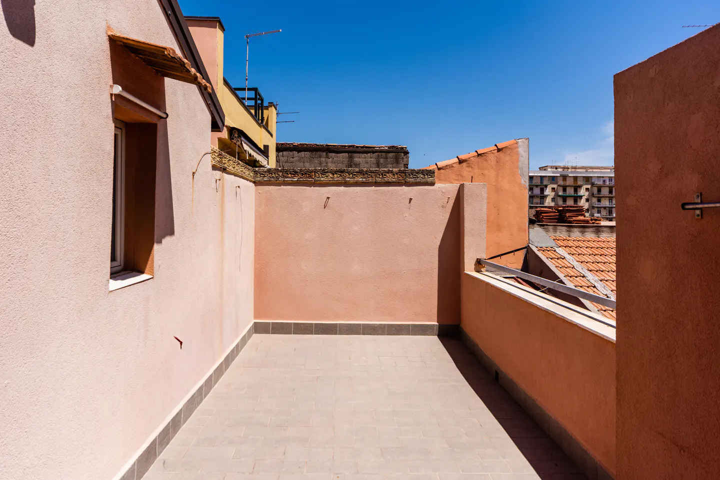 A sunny, tiled rooftop terrace enclosed by light pink and orange stucco walls under a clear blue sky.