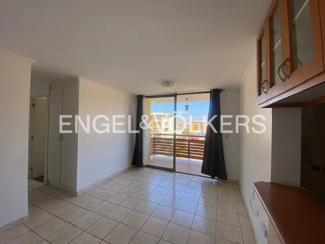 Bright apartment interior with tile floors, sliding glass doors to a balcony, and wood cabinets. Gray curtains frame the balcony view.