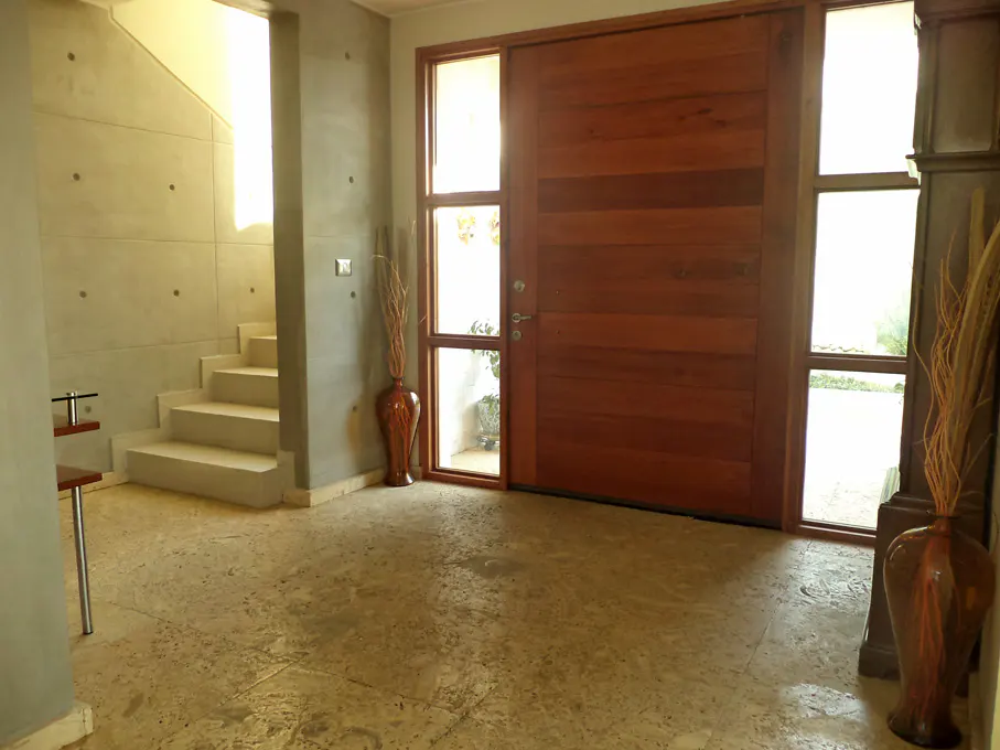 A modern home's foyer with a large wooden door, side windows, and a staircase. Vases with dried branches add a decorative touch.