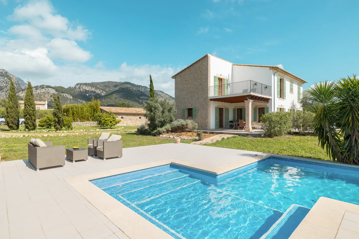 Exterior view of a two-story house with a pool, patio furniture, green lawn, and mountains in the background.