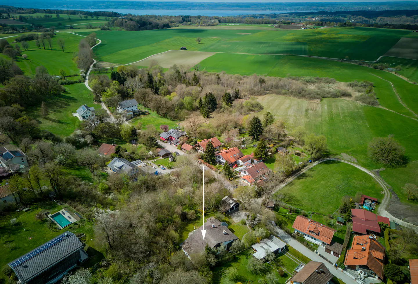 Aerial view of a brown-roofed house with an arrow pointing to it, surrounded by green fields and trees.