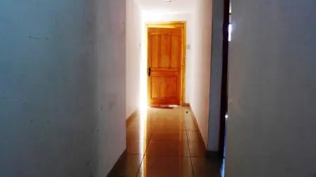 Hallway with white walls and a wooden door at the end, light shining through. Tiled floor reflects the light.