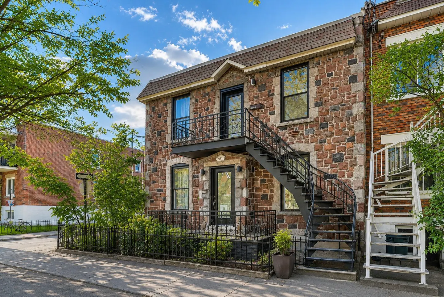 Two-story stone building with black metal stairs leading to the second floor entrance. A black fence surrounds the front of the property.