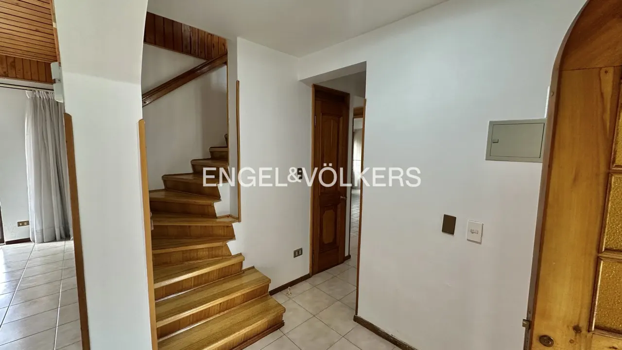 Interior view of a home's entryway with wooden stairs, a door, and white walls. The Engel & Völkers logo is superimposed on the image.