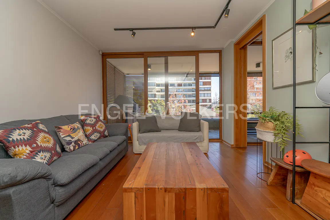 Living room with gray sofa, patterned pillows, and a wooden coffee table on a hardwood floor. Sliding glass doors lead to a balcony.