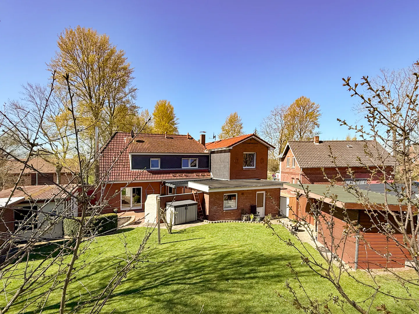 A view of a red brick house with a green lawn and trees under a blue sky.