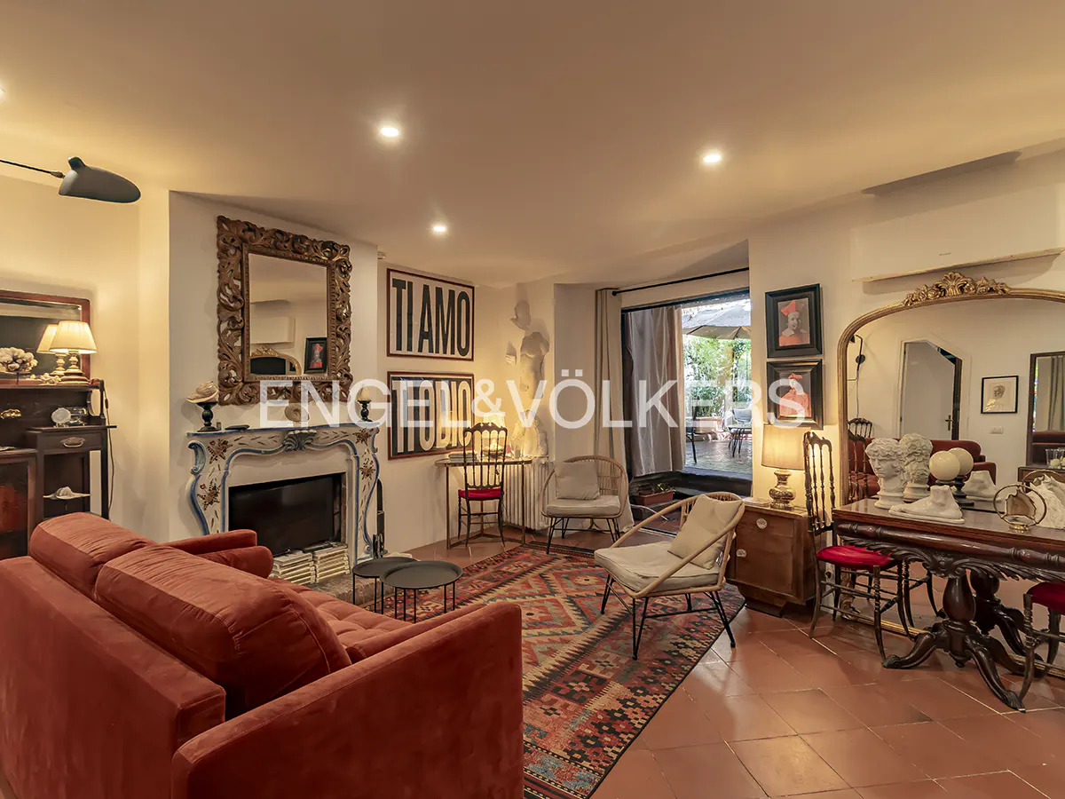 A living room with a red sofa, fireplace, and a large mirror. A patterned rug covers the terracotta floor. "TI AMO" art is on the wall.