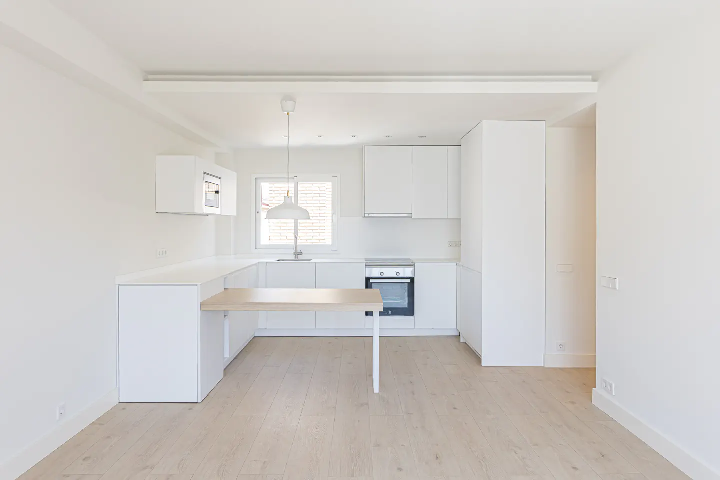 Bright, modern kitchen with white cabinets, countertops, and walls. A light wood table extends from the counter. Hardwood floors and natural light.