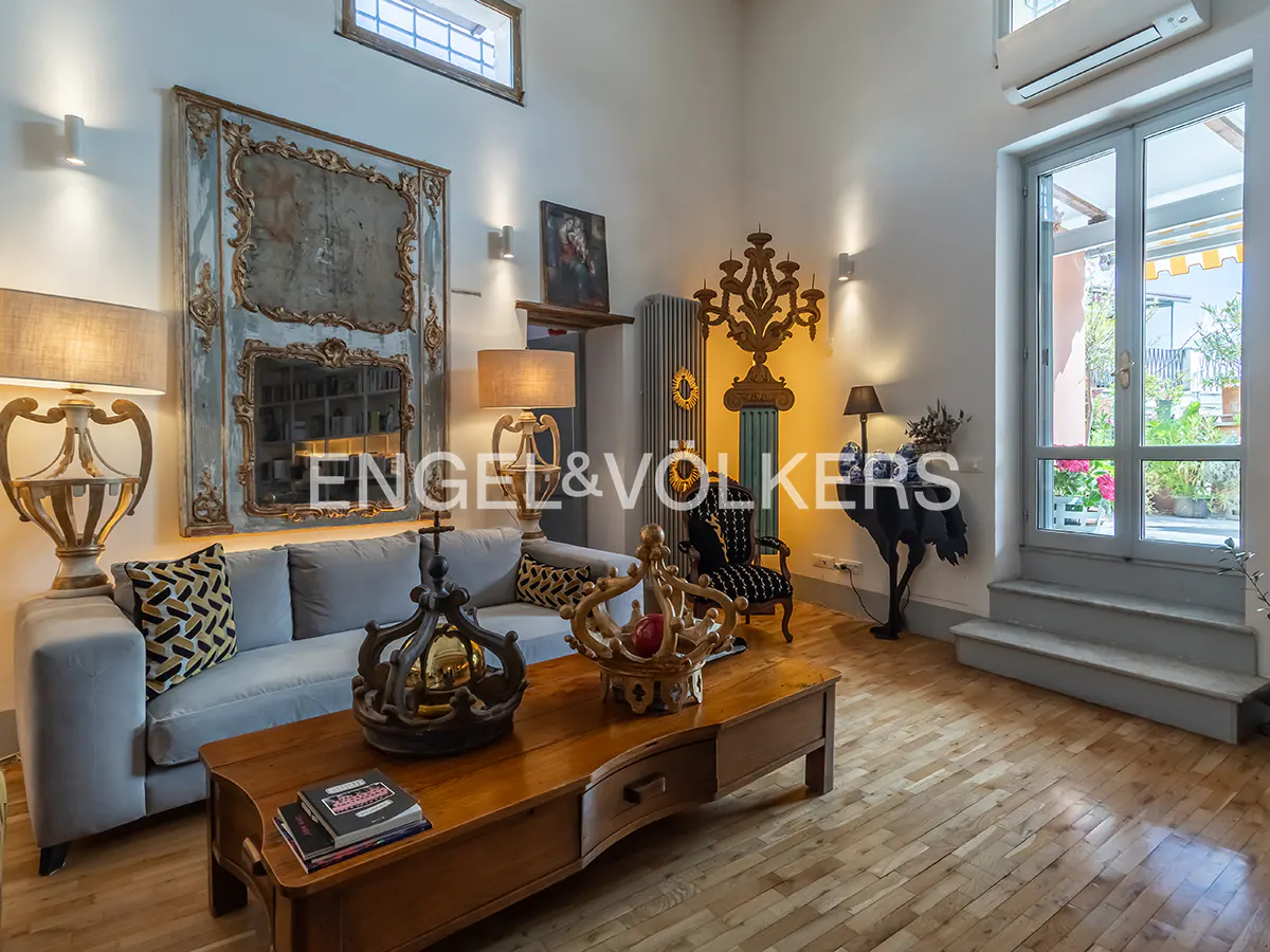 A bright living room with a gray sofa, wooden coffee table, and ornate decor. A large mirror hangs on the wall. French doors lead to a balcony.