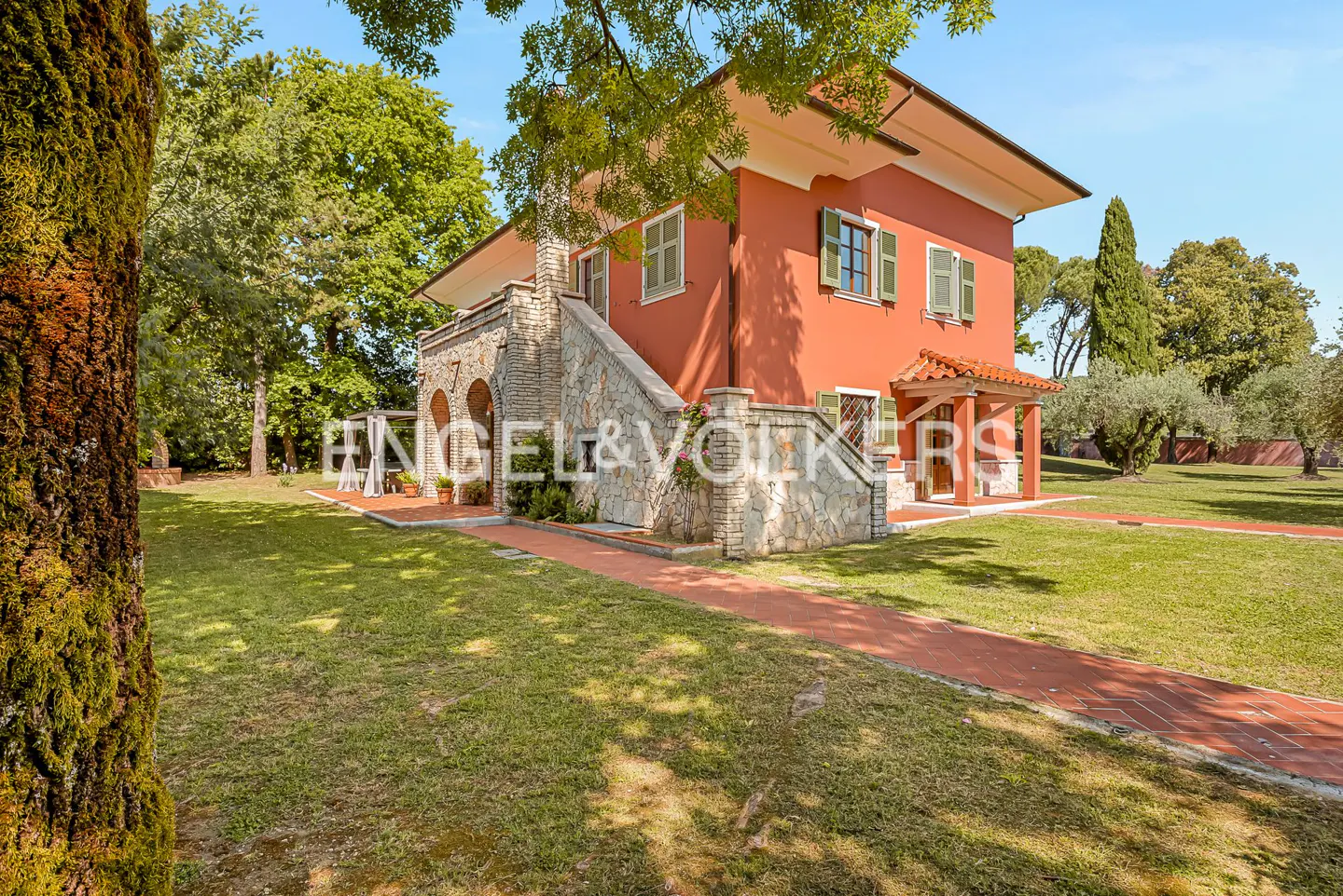 Exterior of a two-story red house with green shutters, stone accents, and a red brick walkway.