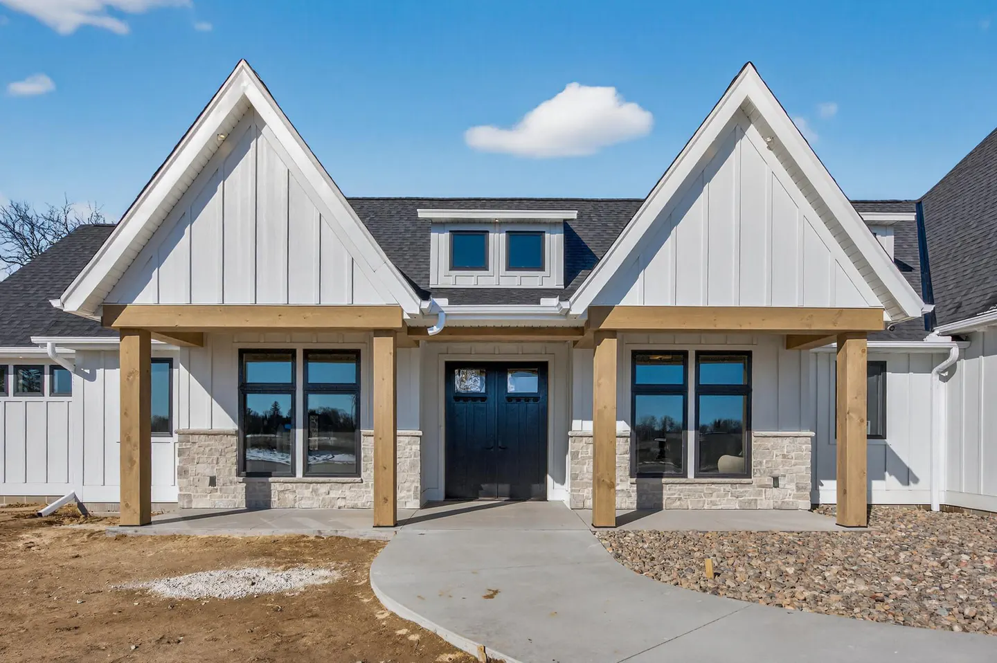Exterior of a white farmhouse-style home with a black front door and a concrete walkway. Blue sky.
